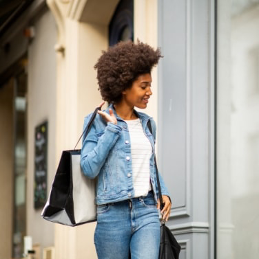 Woman holding shopping bag looking into window of a storefront.